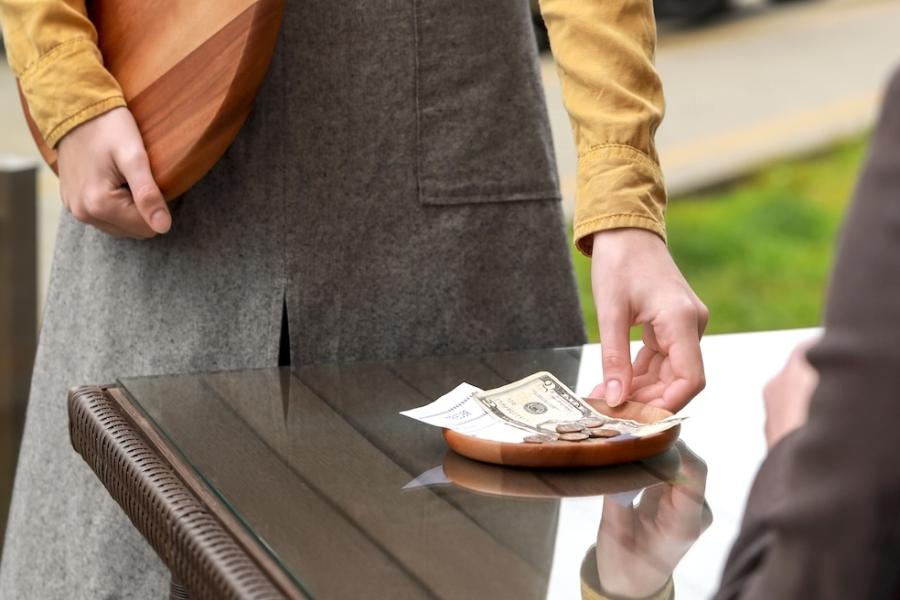 A waitress picks up a small tray that contains a customer’s bill and cash tip.