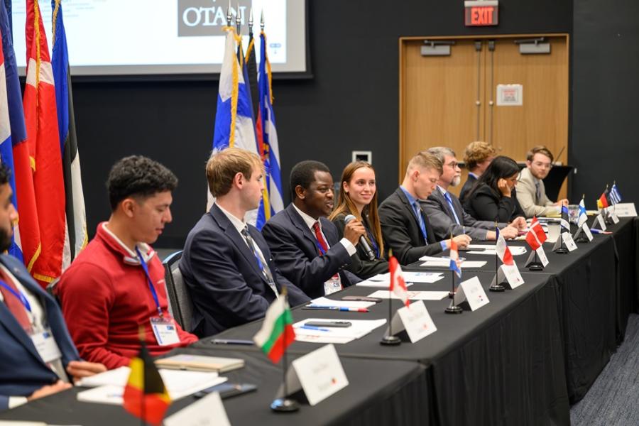 Students sitting in a round table with international flags behind them