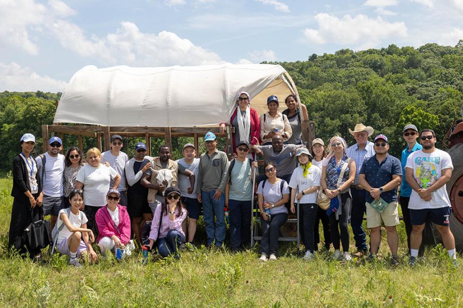 Fellows in the Hubert H. Humphrey program standing in a field in front of a covered wagon.