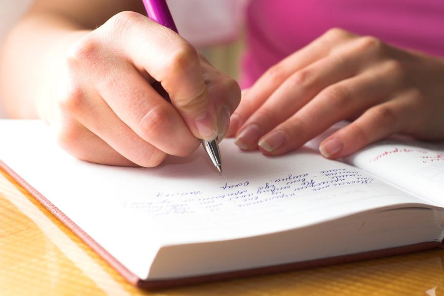 An image of a young person's hands, writing in a journal.