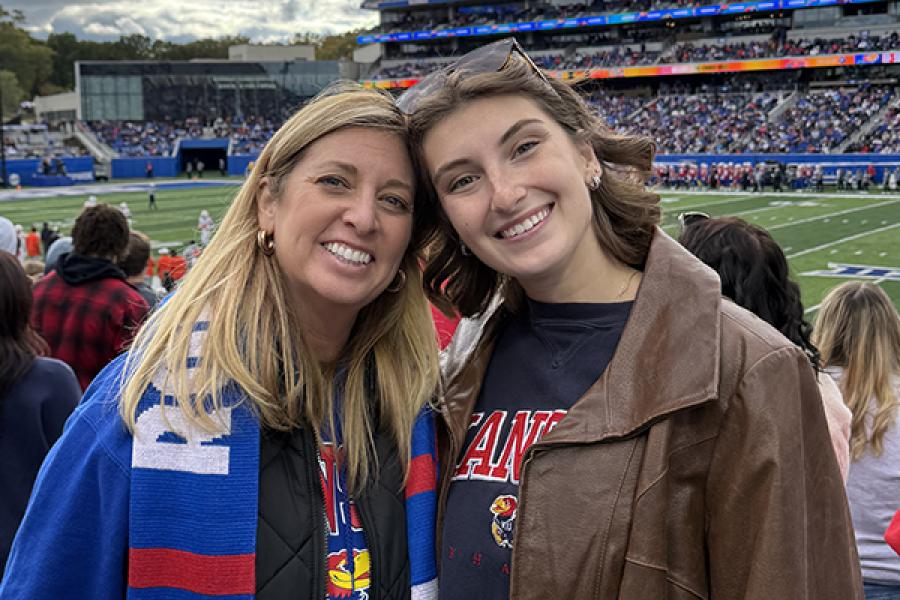 Two women stand in a football stadium smiling