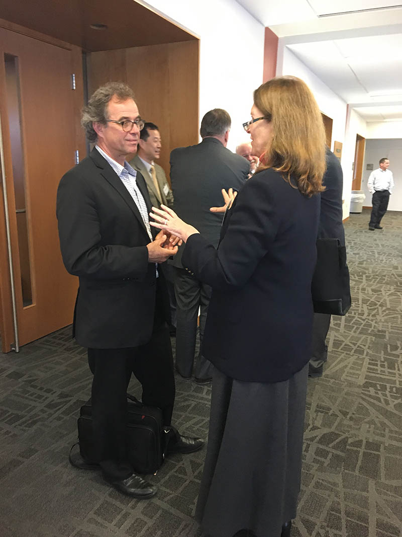 Two individuals engaged in conversation in a lobby, with others in the background.