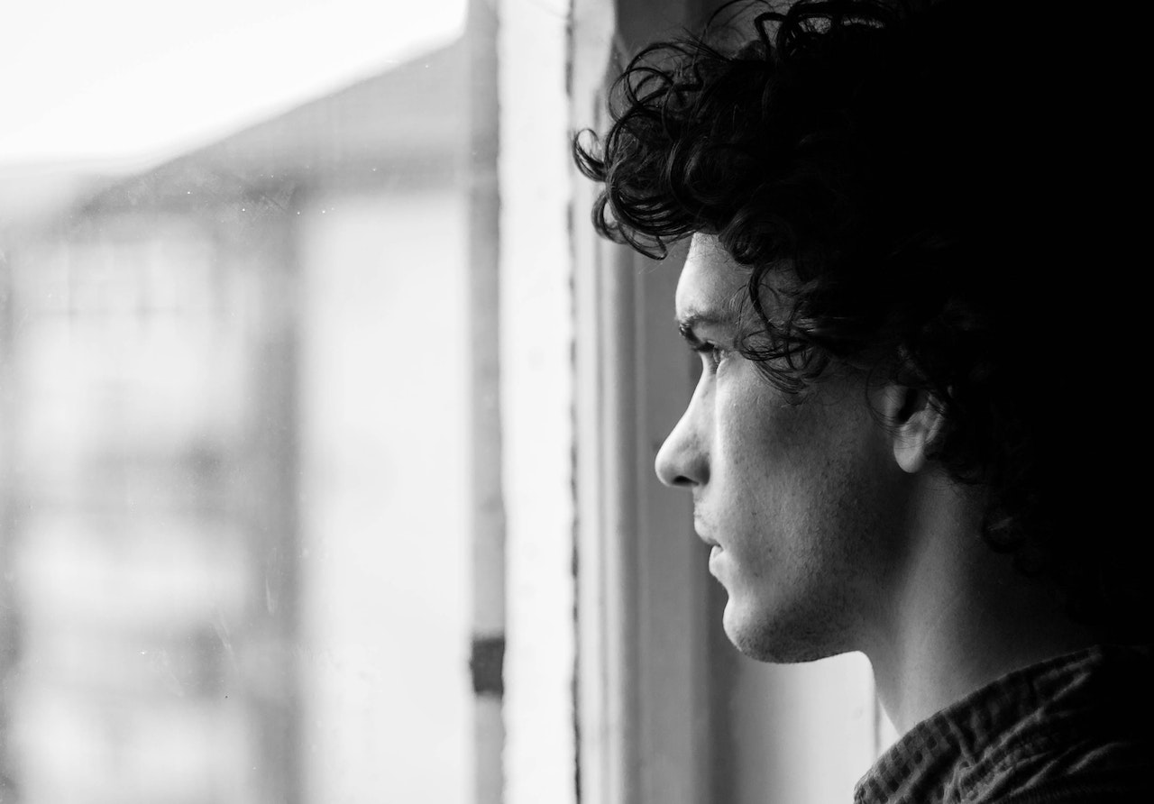 Black/white image of individual staring out window. Credit: Pexels