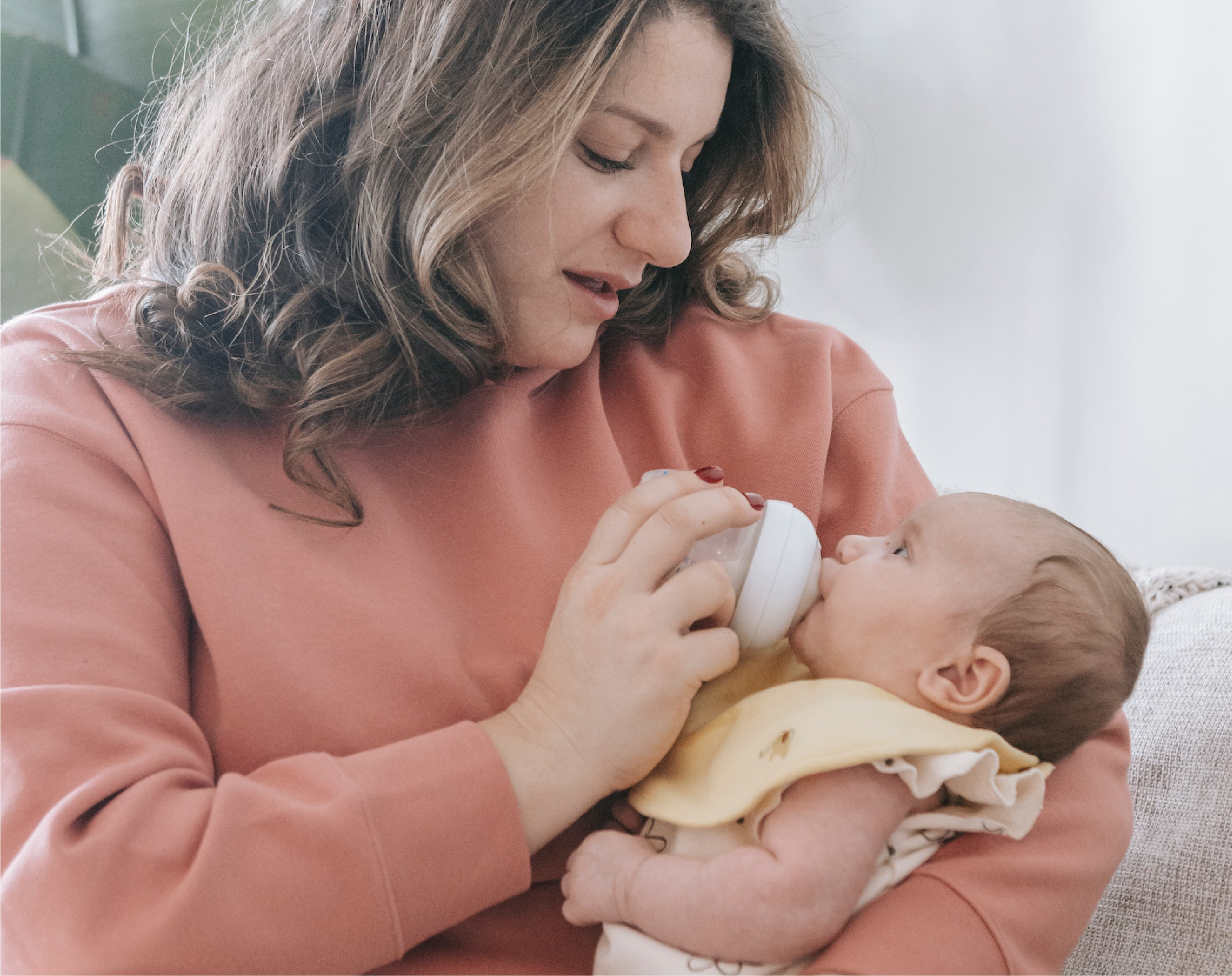 "A woman feeds a baby a bottle she holds in her lap"