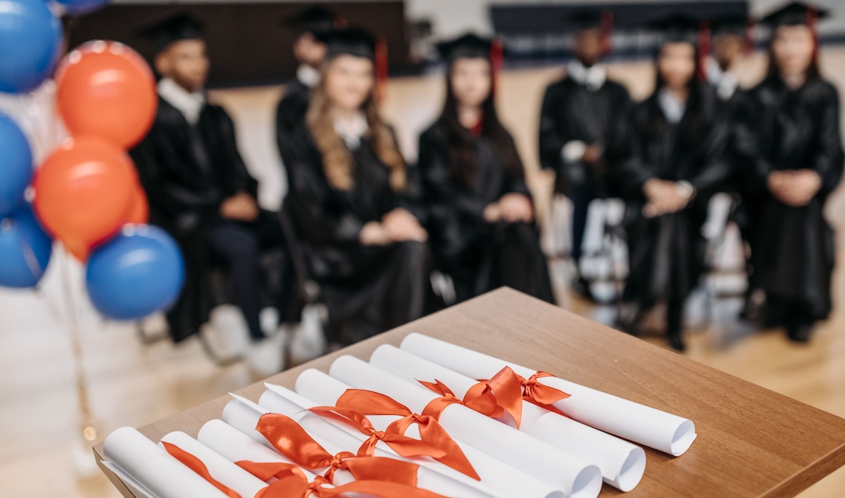 stack of diplomas with graduates in the background