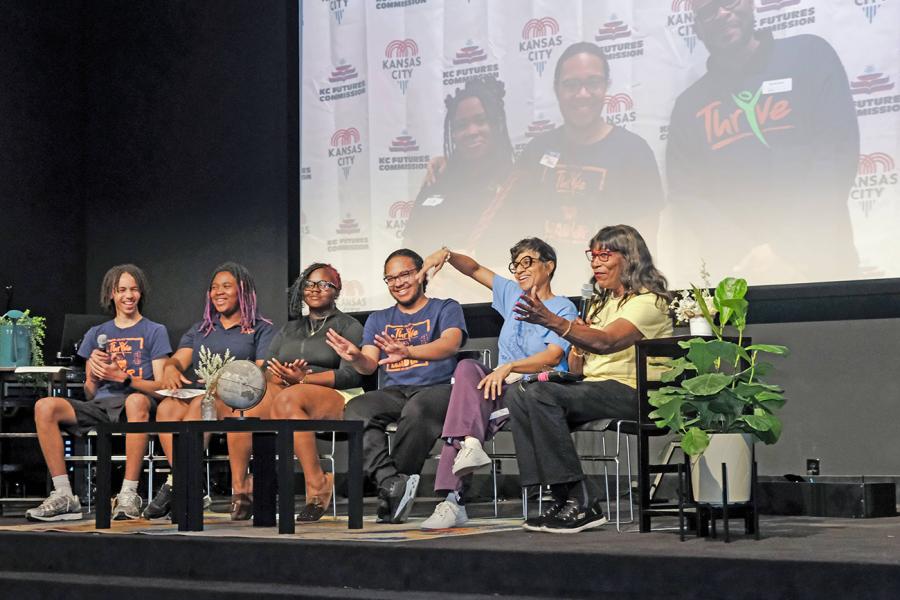 A panel of adults and youth speak in front of an audience at a community event.