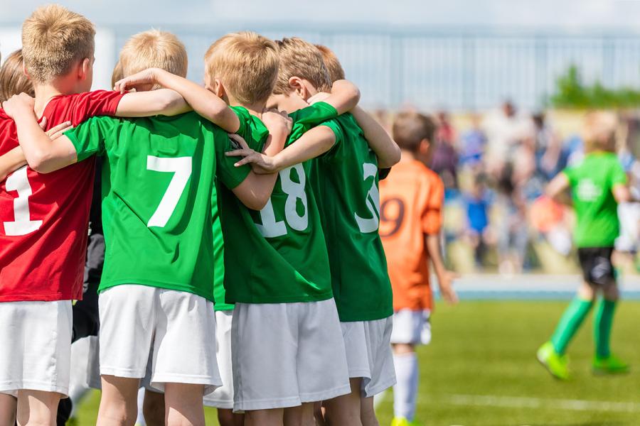 A group of young soccer players huddle on the field of play.